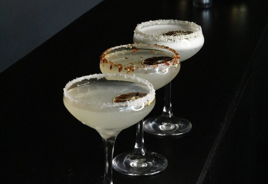 Three margaritas with salted rims along the bar