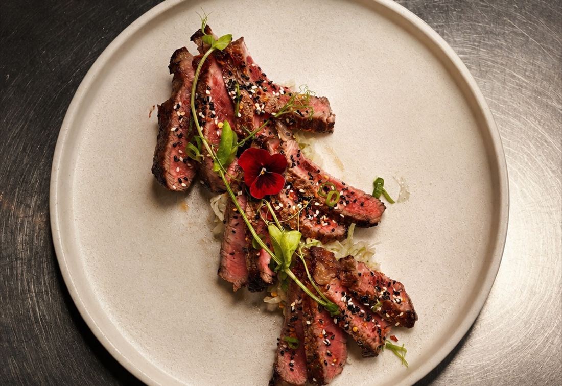 Sliced wagyu fanned across a plate with sesame and micro herbs